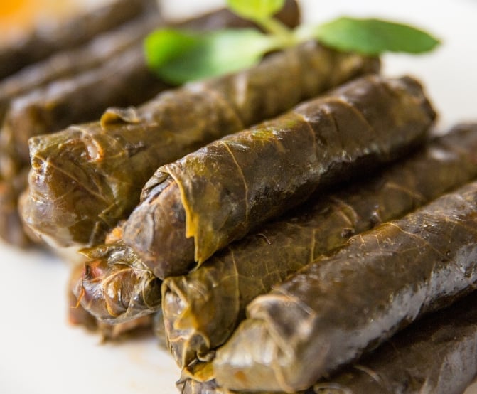 Rolled grape leaves filled with rice and herbs, arranged on a white plate with fresh mint garnish
