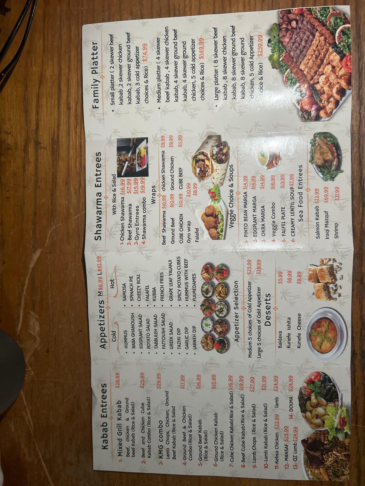 Restaurant menu on wooden table with sections for Family Platters, Sizzling Entrees, Appetizers, Kebab Entrees, and Desserts